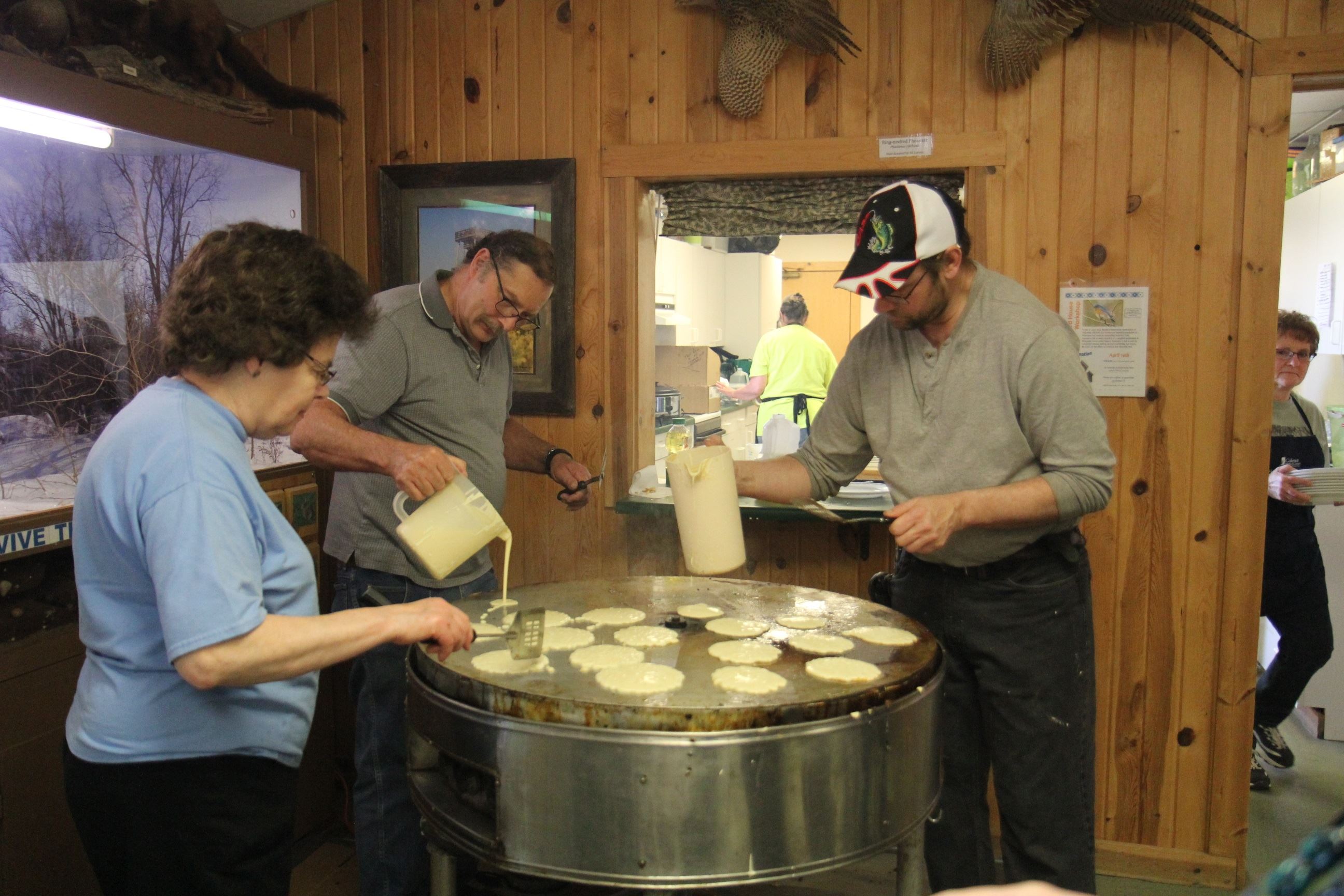 3 people pouring pancake batter onto a large round cooker