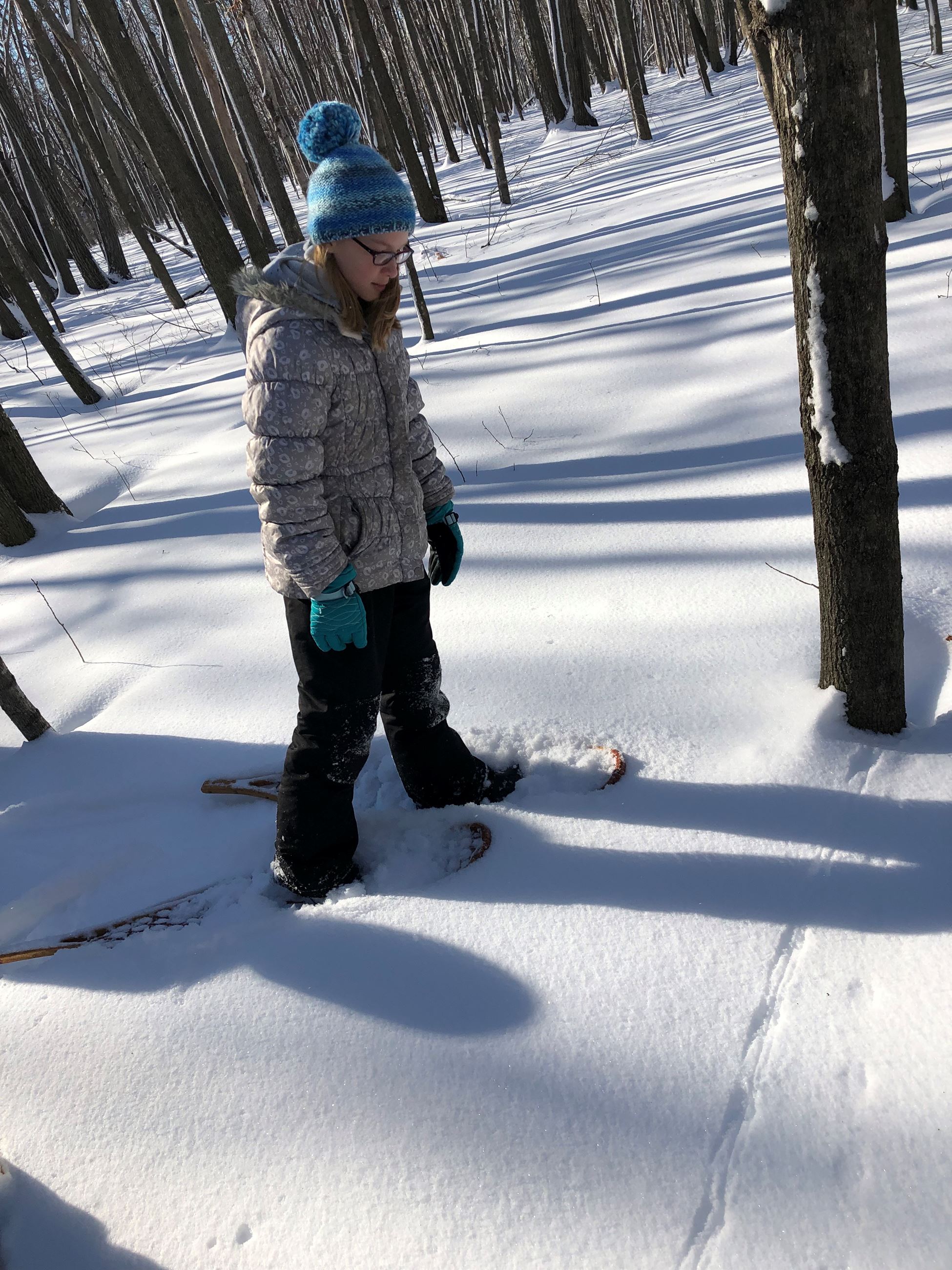 a girl on snowshoes looking at animal tracks in the snow