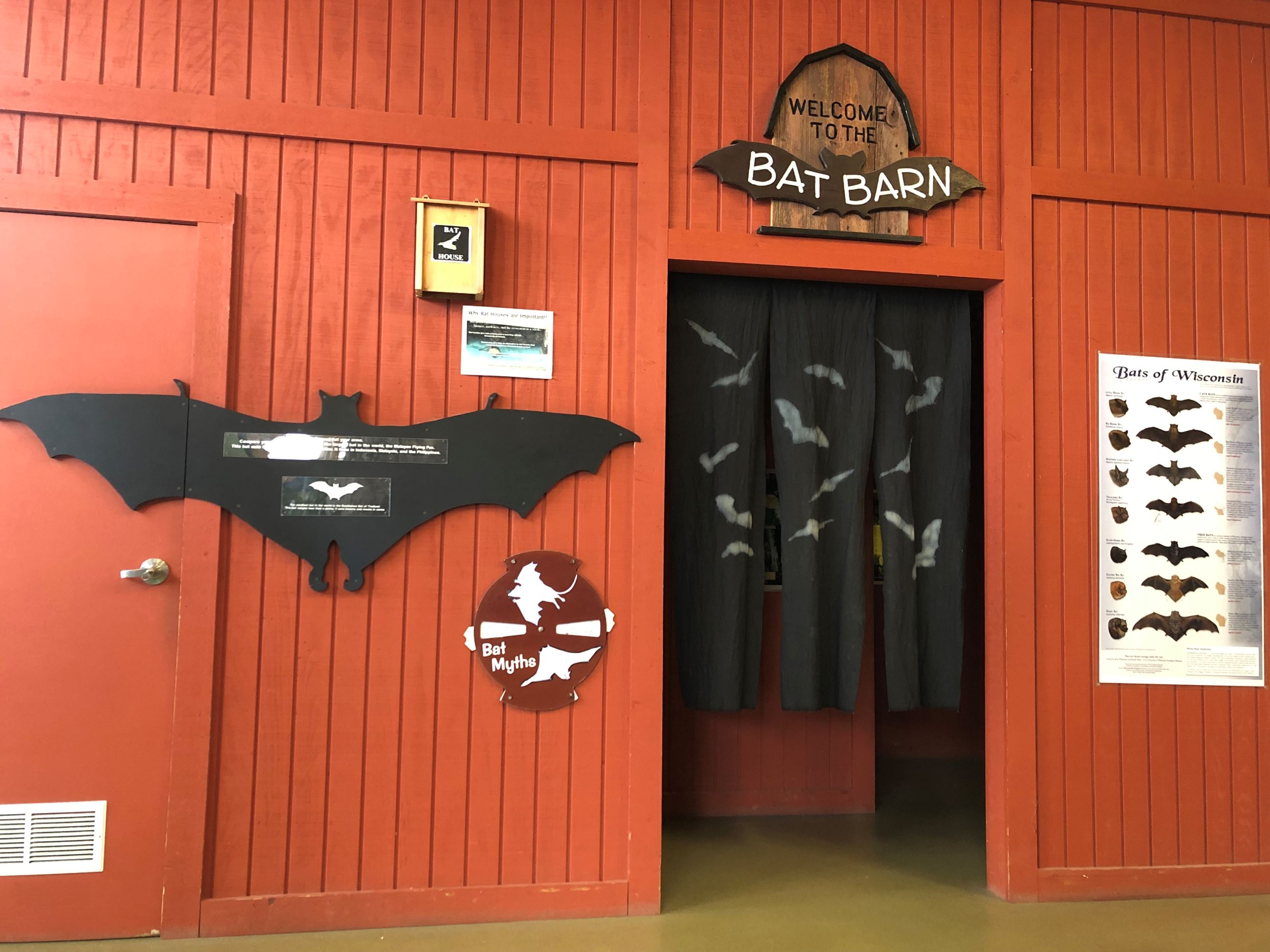 A red wooden wall that has a sign that says Bat barn on it. There is a large black cutout of a bat o