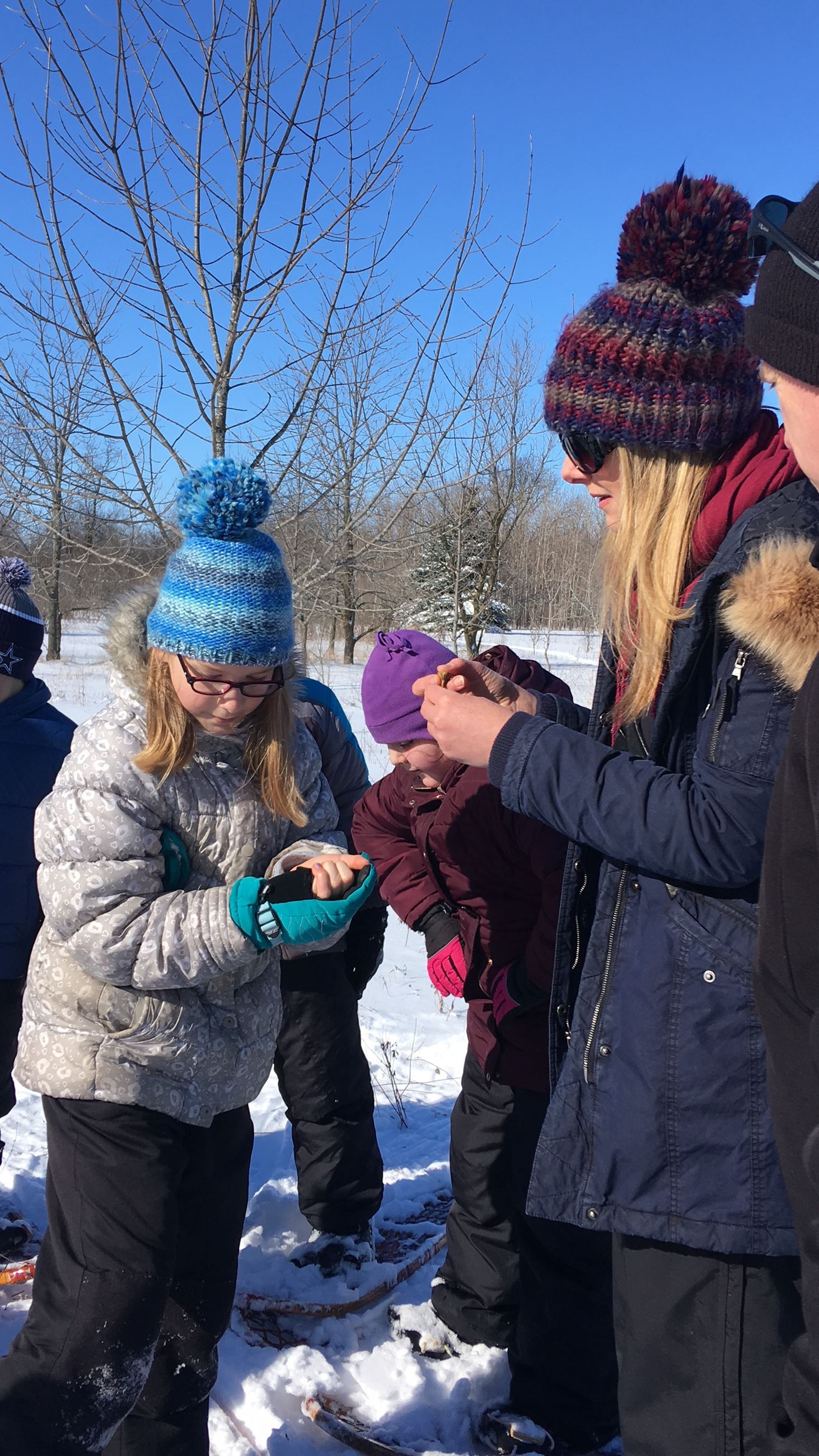 A girl and a woman outside in the snow. They are wearing coats and hats and looking at something in 
